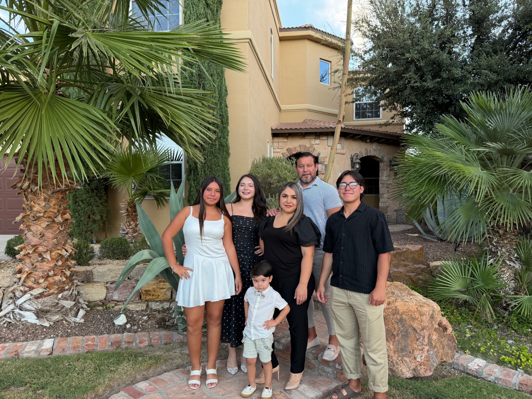 Family standing in front of a stucco home with palm trees in El Paso