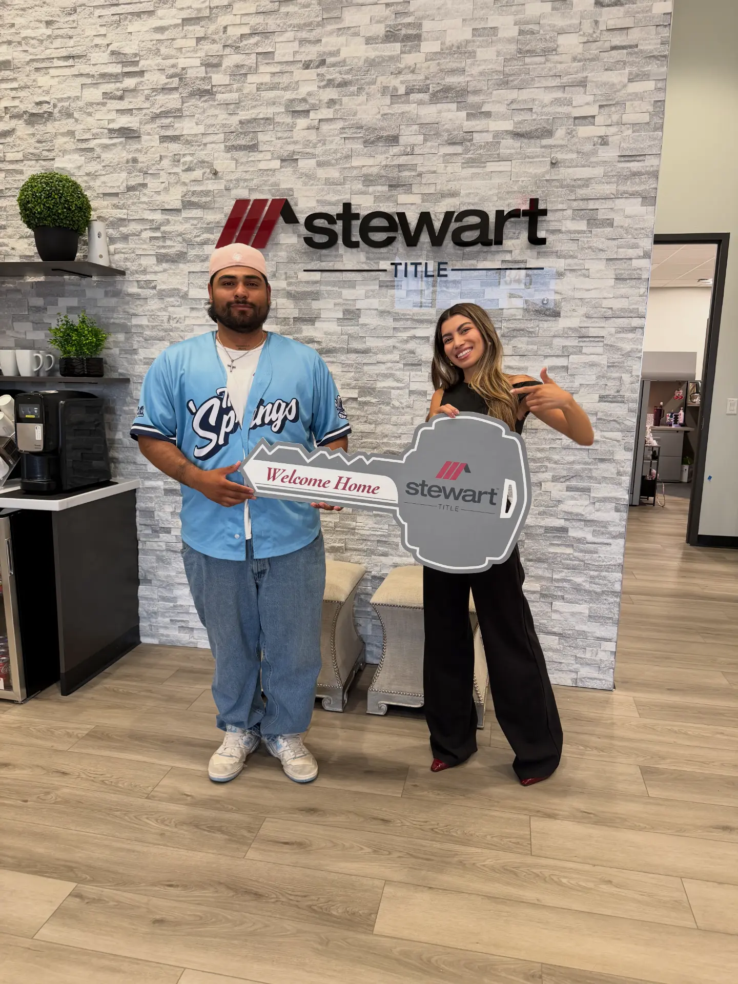 First-time home buyers holding a giant Welcome Home key at the title company