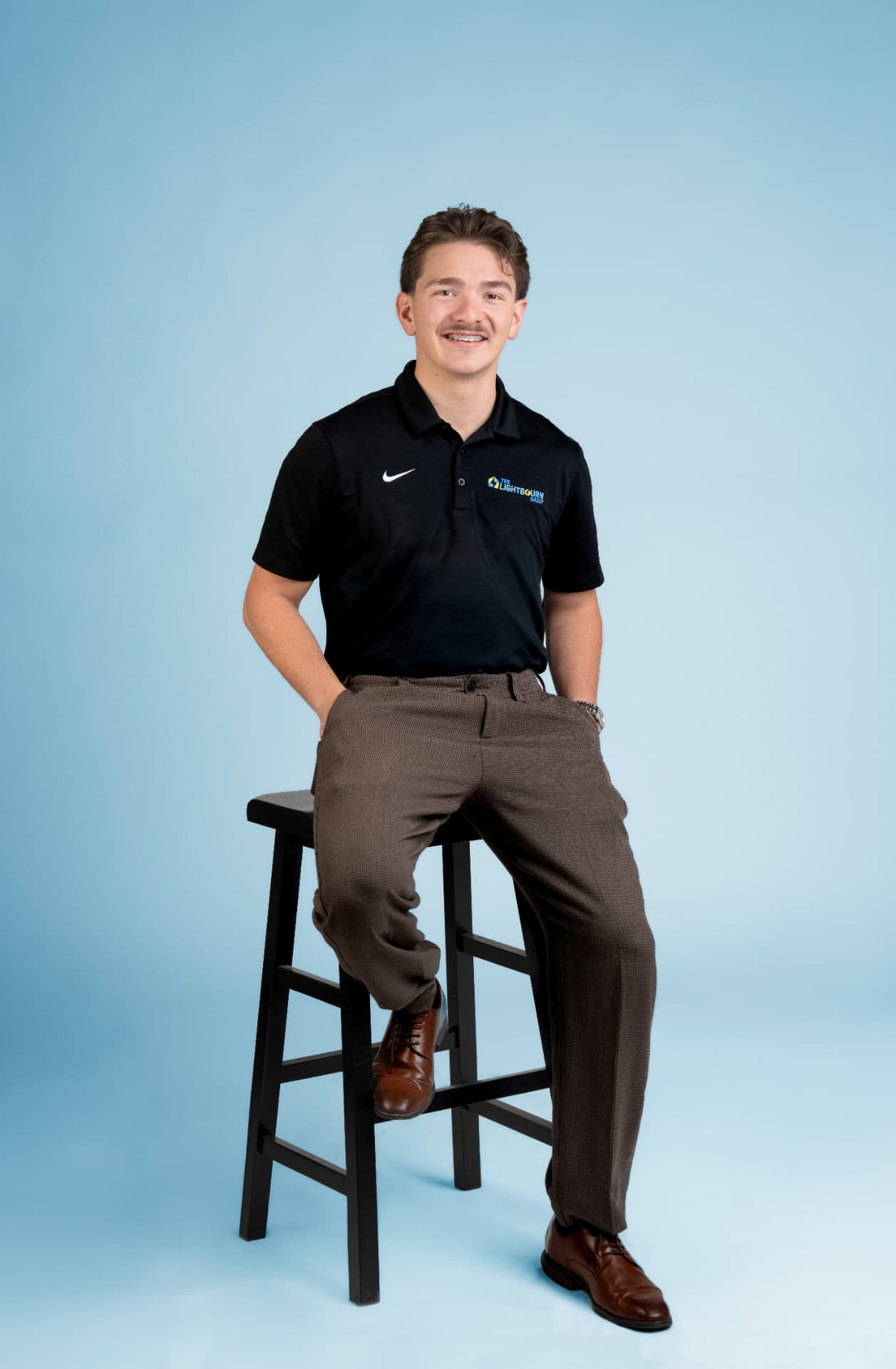 Isacc Lightbourn, founder of The Lightbourn Group, sitting on a stool against a blue backdrop