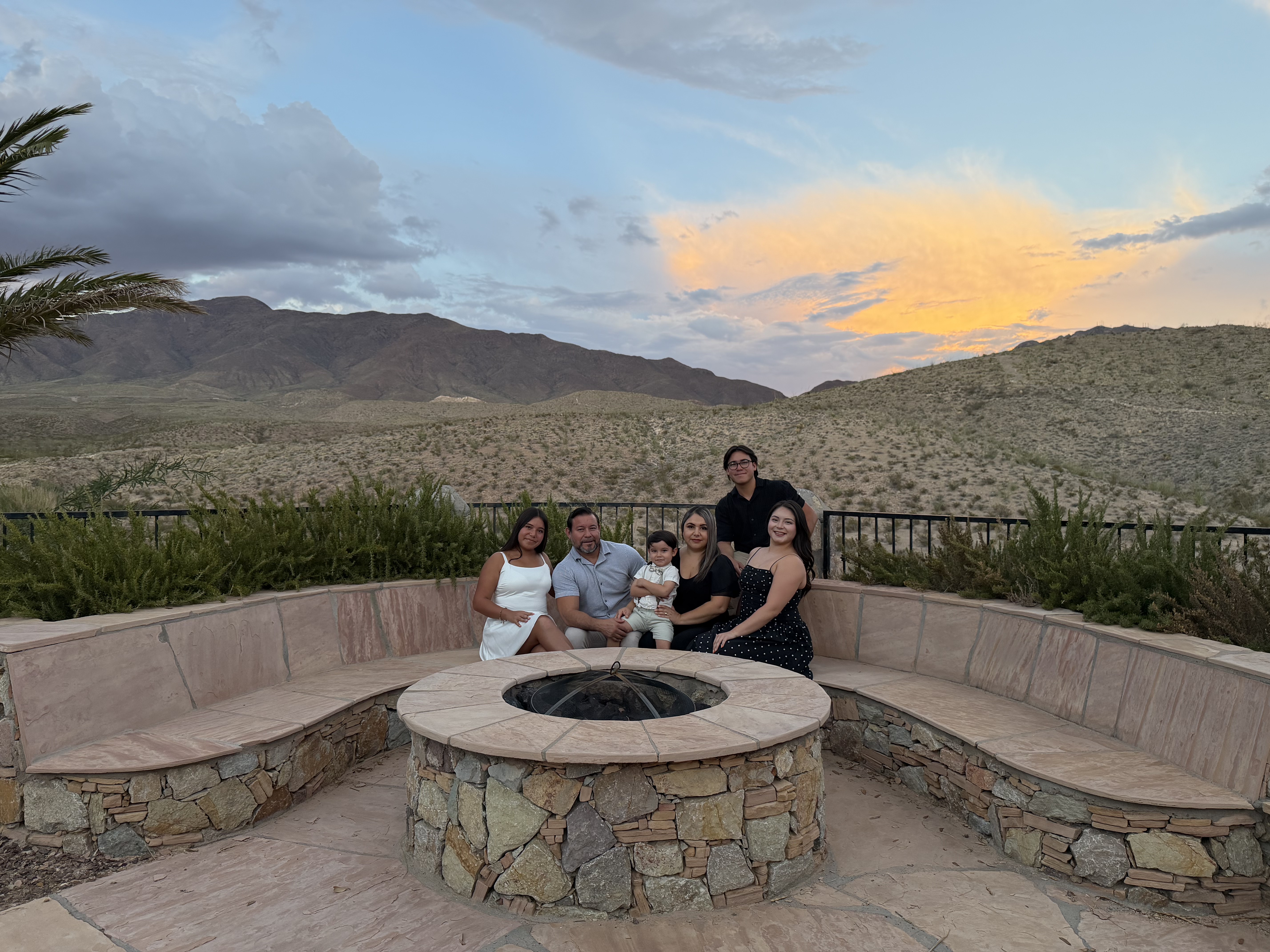 Family gathered around a stone fire pit with El Paso mountain views at sunset